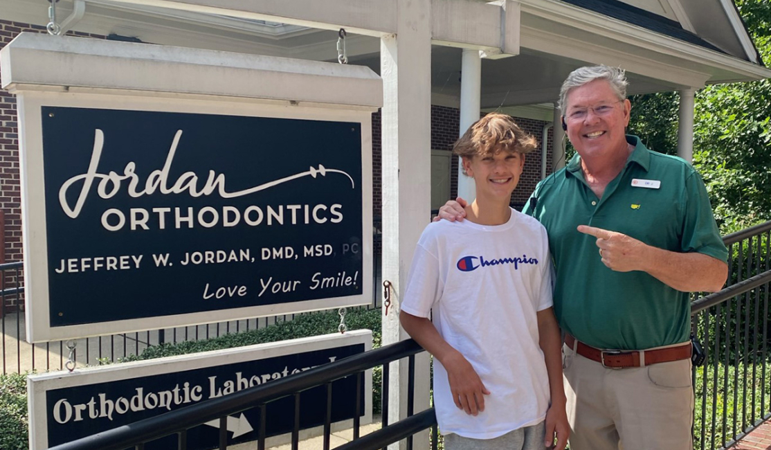 Dr. Jordan with teenage boy patient in front of Jordan Orthodontics sign in Alpharetta, Georgia
